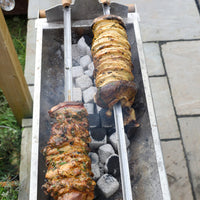 vegatable and chicken rotisserie of meat cooking on a small grill outdoors.