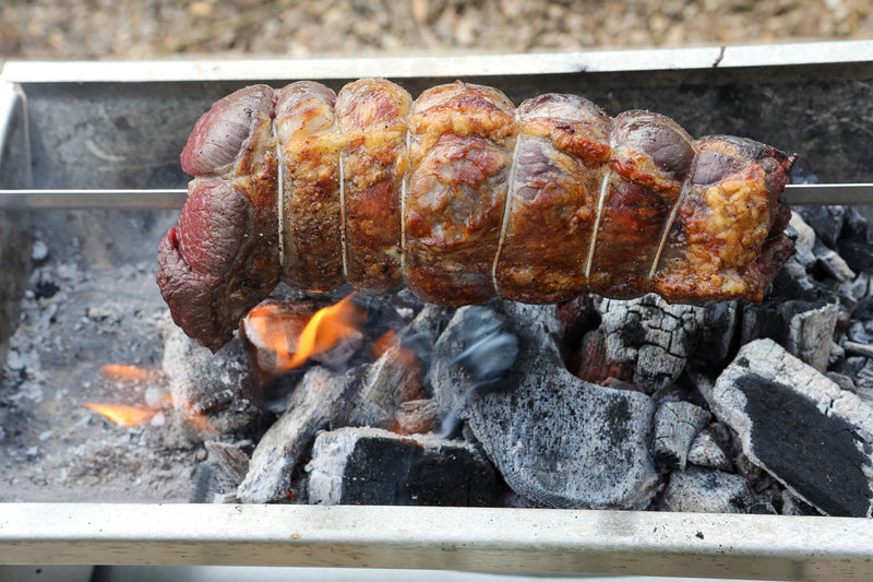 Meat on a rotisserie over an open flame on a grill Rozza BBQ