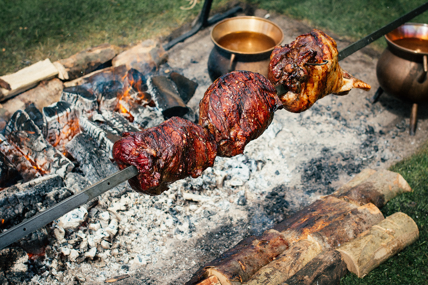 Meat skewer over an open fire with cooking pots in the background