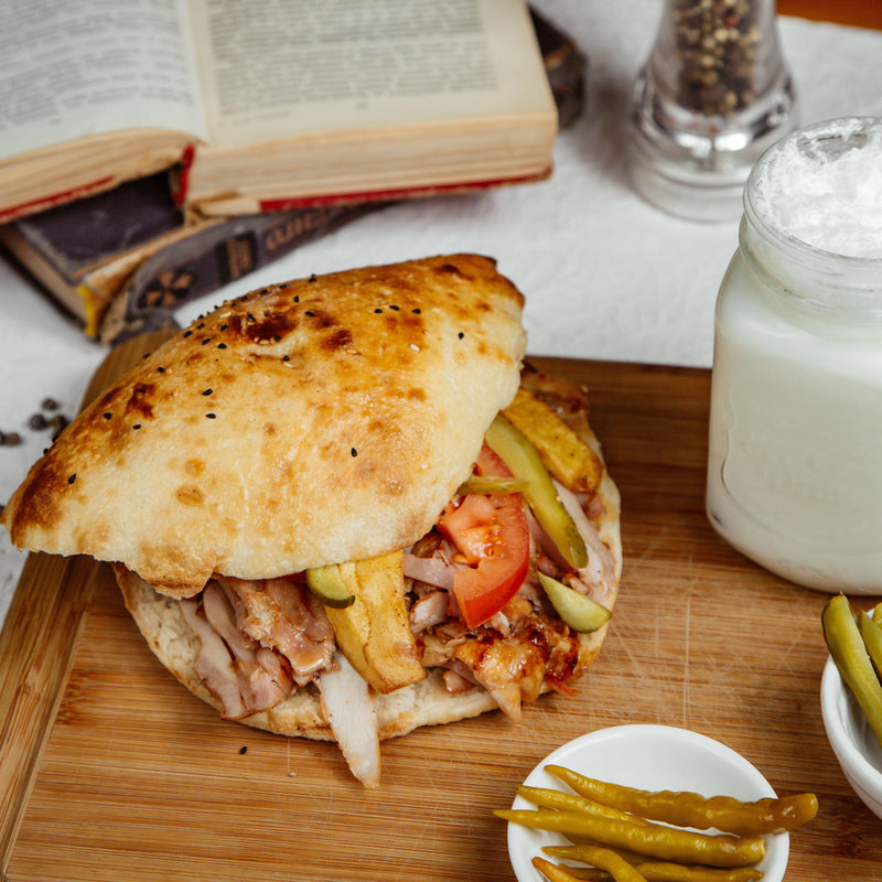 Gyros with chicken, tomatoes, and pickles on a wooden cutting board with a glass of milk and books in the background.