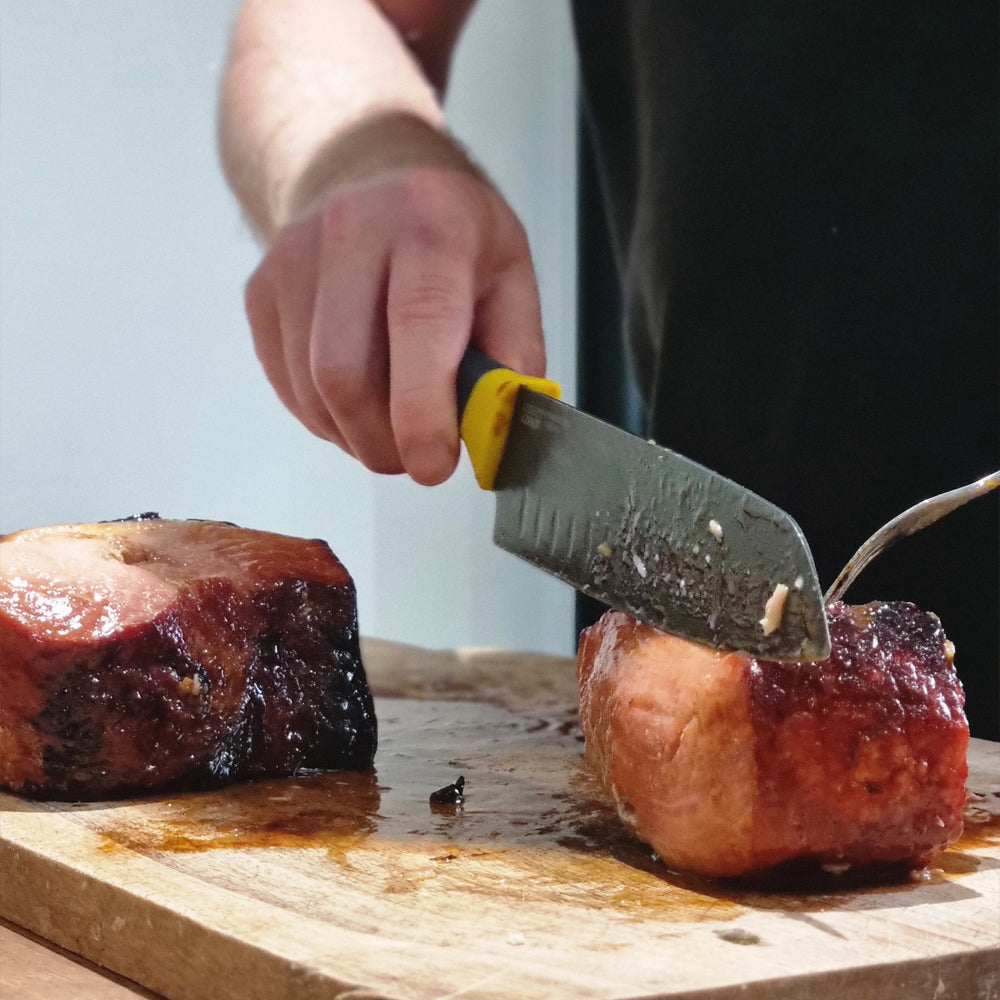 Person cutting a piece of meat on a wooden board with a knife.