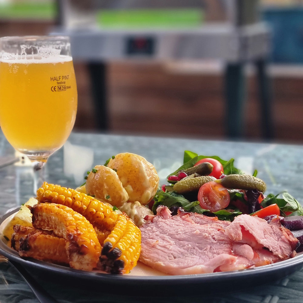 Plated meal with corn, salad, and meat next to a glass of beer on a table.