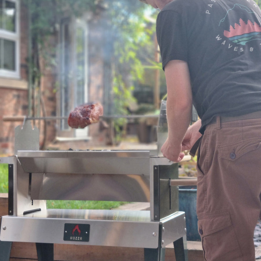 Man grilling outdoors using the Rozza with a piece of meat on a skewer.