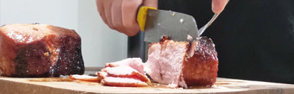 Person slicing a piece of meat on a wooden cutting board with a knife.
