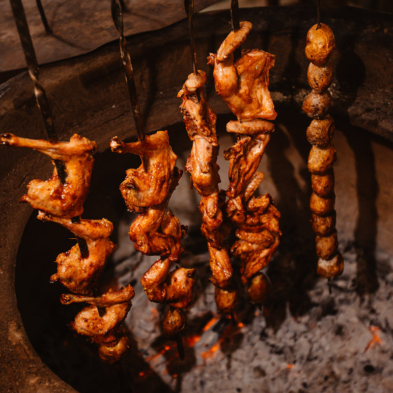 Skewered meats being cooked over an open flame in a traditional oven.