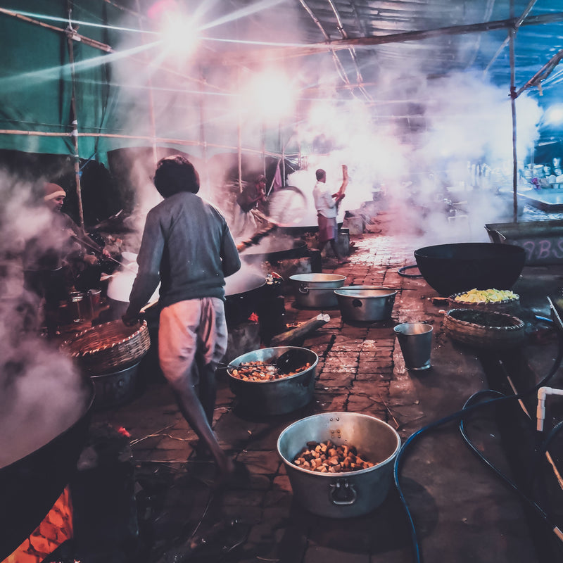 People working in a kitchen with large pots and steam